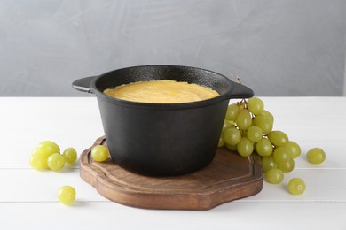 Fondue with tasty melted cheese and grapes on white wooden table