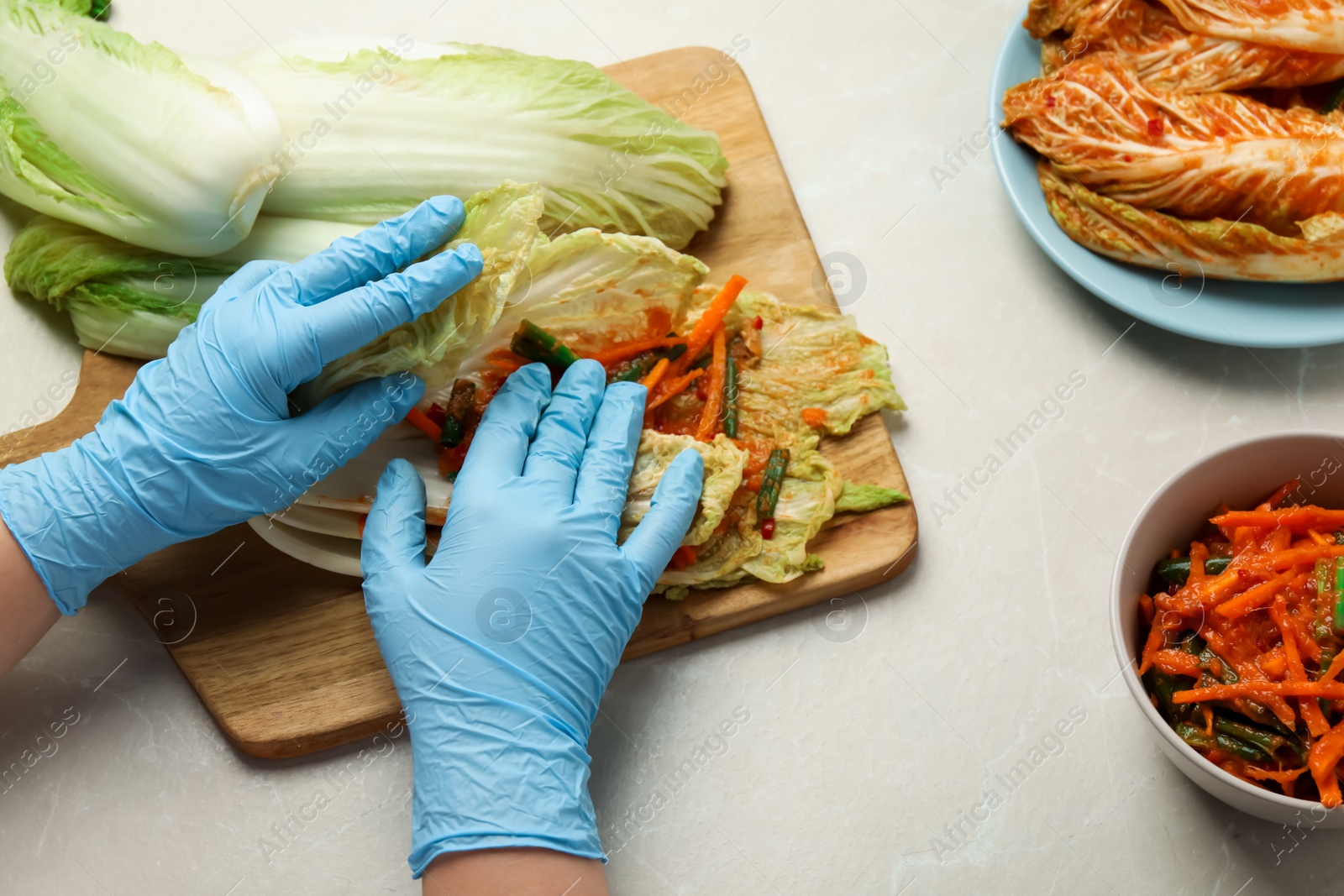 Photo of Woman preparing spicy cabbage kimchi at beige marble table, above view
