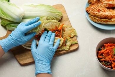 Woman preparing spicy cabbage kimchi at beige marble table, above view