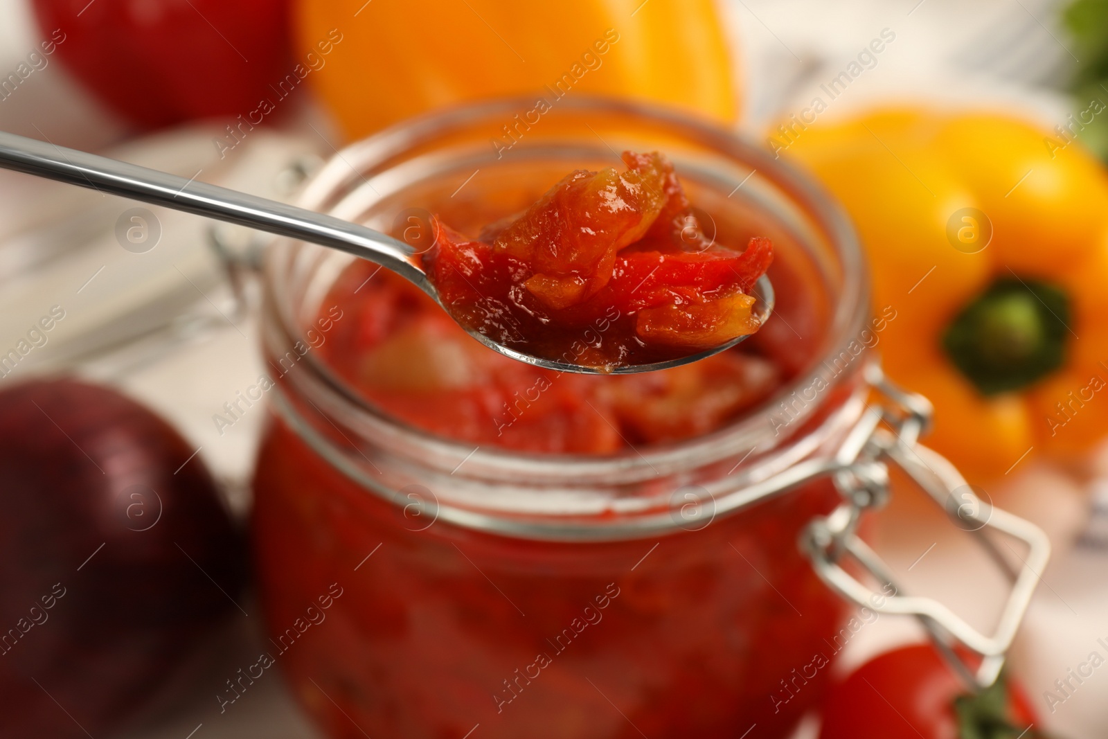 Photo of Spoon with delicious lecho over jar, closeup