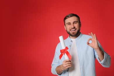 Photo of Happy student with diploma on red background. Space for text