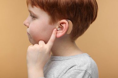 Photo of Little boy with hearing aid on pale brown background, closeup