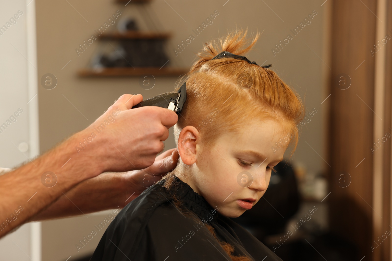 Photo of Professional hairdresser cutting boy's hair in beauty salon, closeup