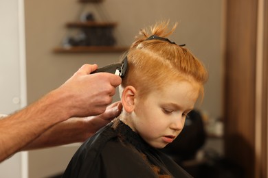 Photo of Professional hairdresser cutting boy's hair in beauty salon, closeup