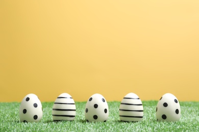 Photo of Line of traditional Easter eggs decorated with black paint on green lawn against color background, space for text