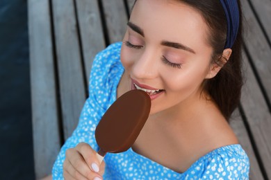 Photo of Beautiful young woman eating ice cream glazed in chocolate on pier, closeup