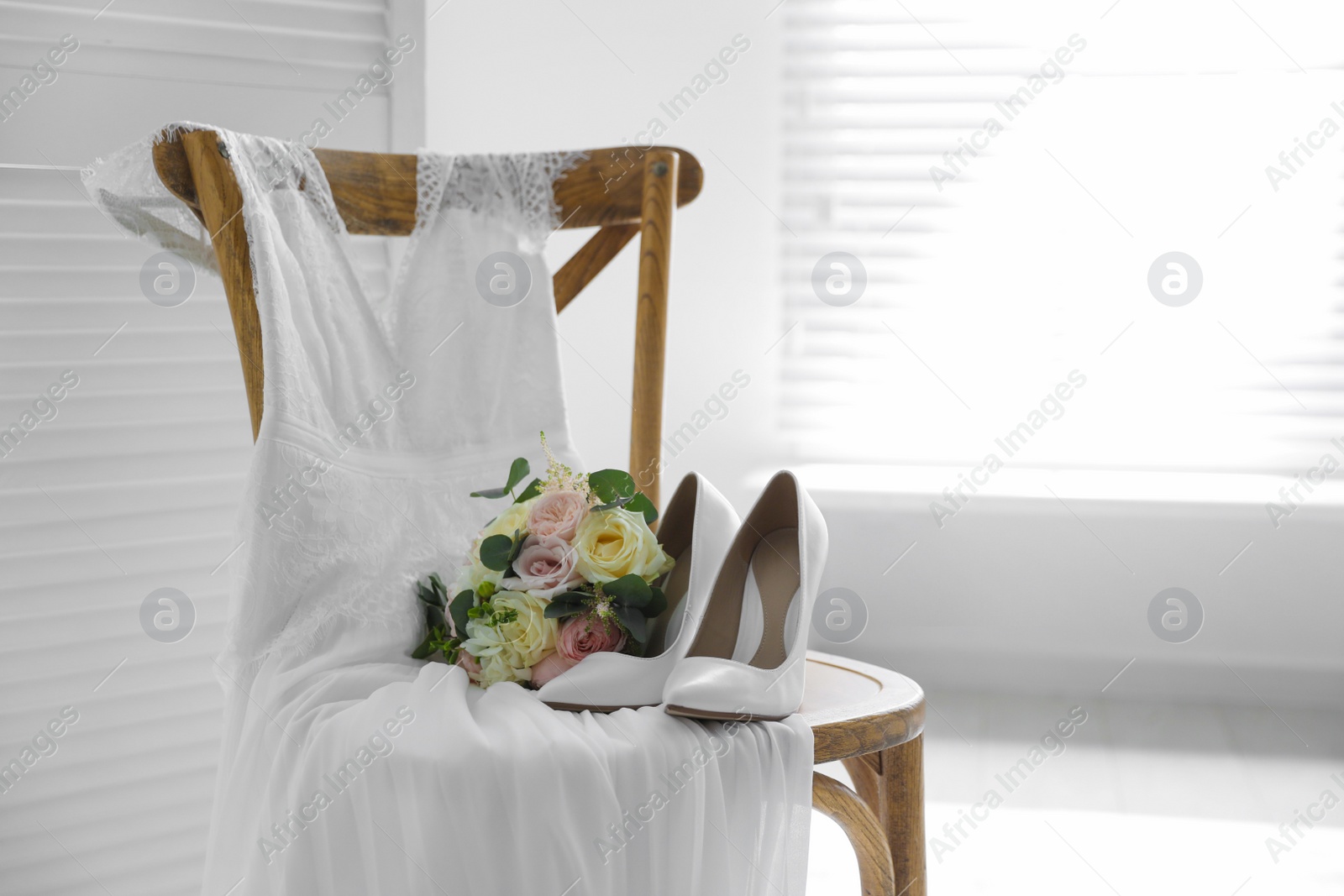 Photo of White high heel shoes, flowers and wedding dress on wooden chair indoors. Space for text