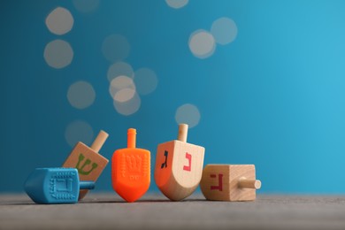 Photo of Different dreidels on wooden table against light blue background with blurred lights, space for text. Traditional Hanukkah game