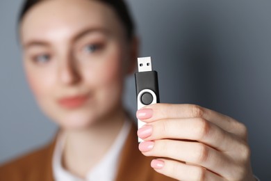 Woman holding usb flash drive against grey background, focus on hand