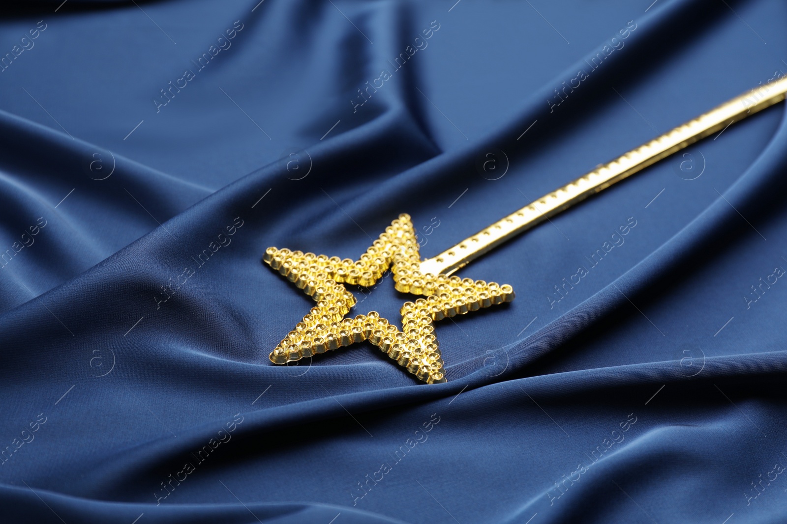 Photo of Beautiful golden magic wand on blue fabric