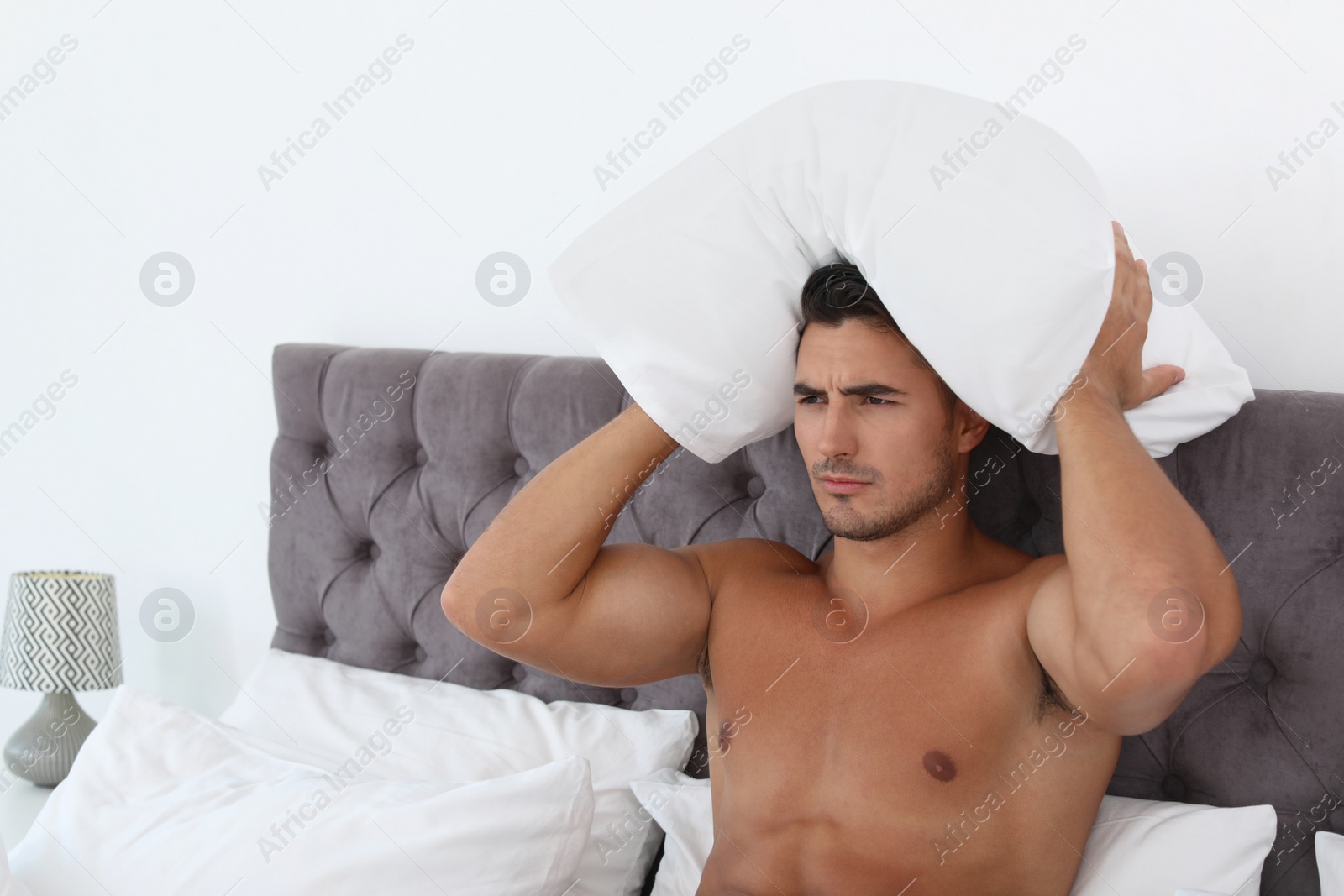 Photo of Emotional young man with soft pillow on bed at home