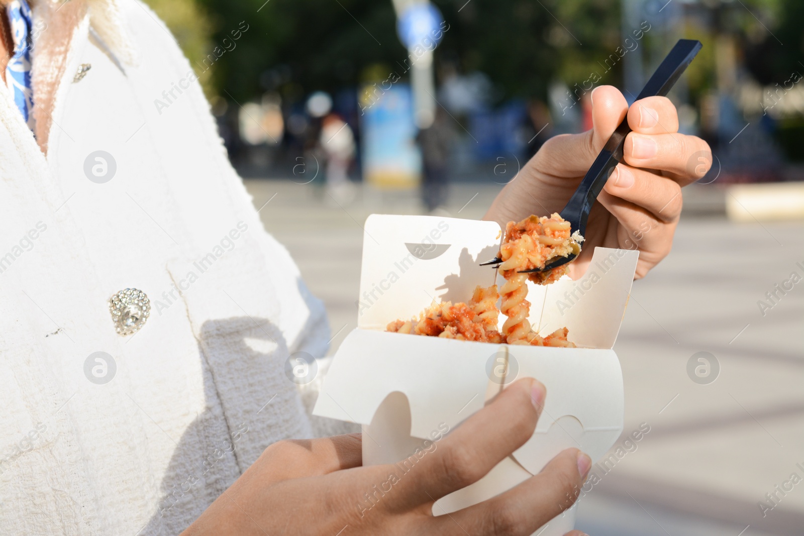 Photo of Woman eating takeaway noodles from paper box with fork outdoors, closeup. Street food