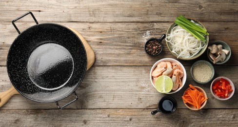 Flat lay composition with black wok, spices and products on wooden table