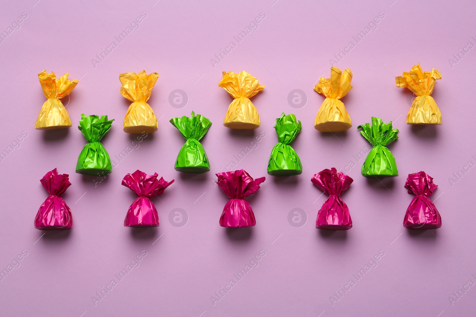 Photo of Candies in colorful wrappers on pink background, flat lay