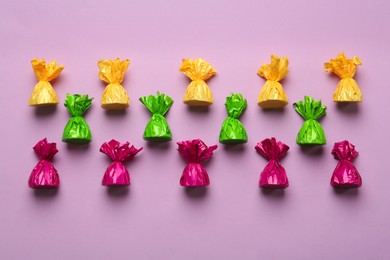 Photo of Candies in colorful wrappers on pink background, flat lay