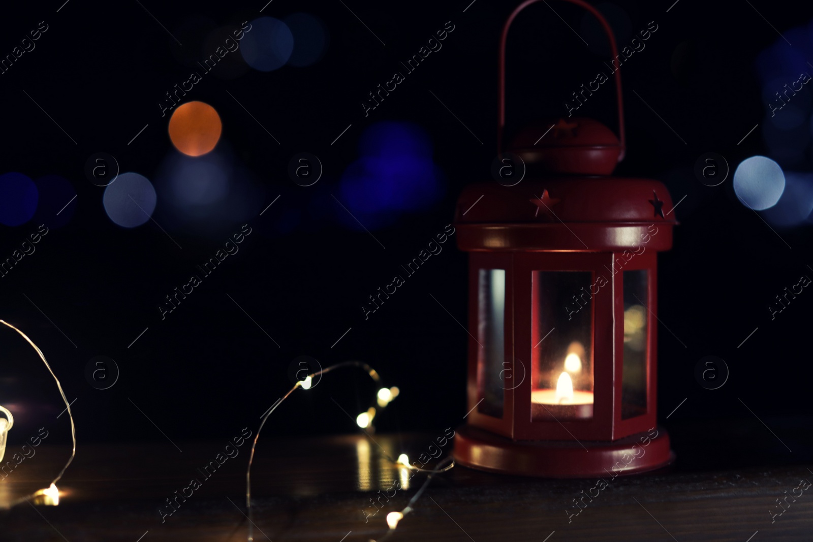 Photo of Lantern and Christmas lights on wooden railing outdoors against blurred background, space for text. Winter night