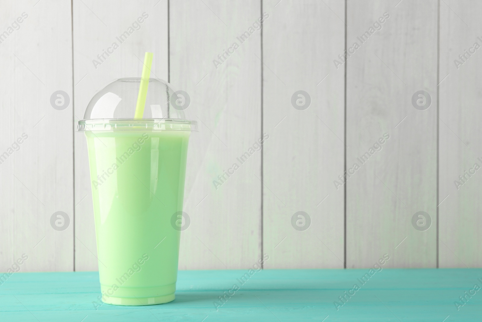 Photo of Tasty smoothie in plastic cup on light blue table against white wooden wall. Space for text