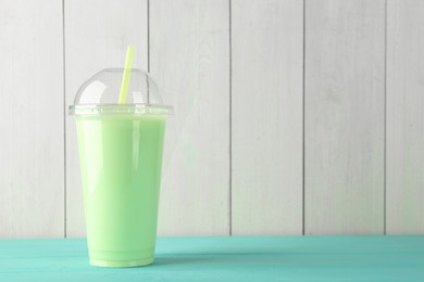 Photo of Tasty smoothie in plastic cup on light blue table against white wooden wall. Space for text