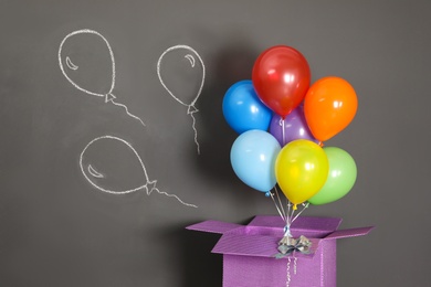 Photo of Gift box with bright air balloons and chalk drawing on grey background