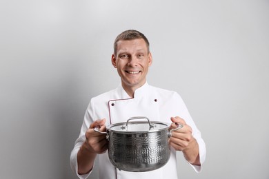Happy male chef with cooking pot on light grey background