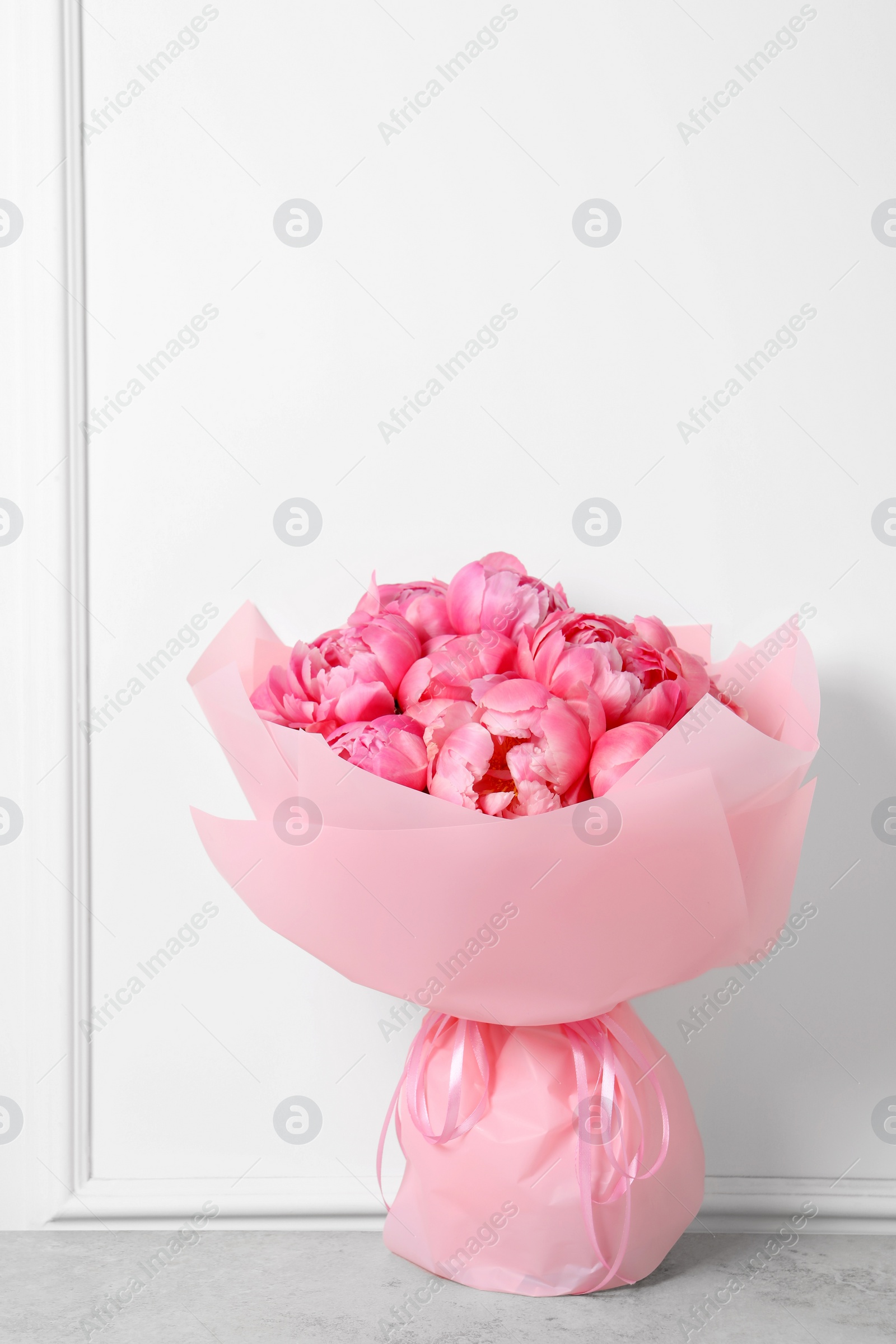 Photo of Bouquet of beautiful pink peonies on table near white wall