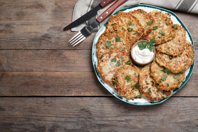 Delicious zucchini fritters with sour cream served on wooden table, flat lay. Space for text