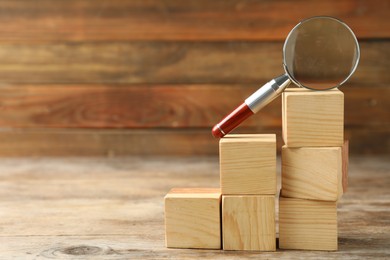 Photo of Magnifier glass and stairs made with cubes on wooden background, space for text. Find keywords concept