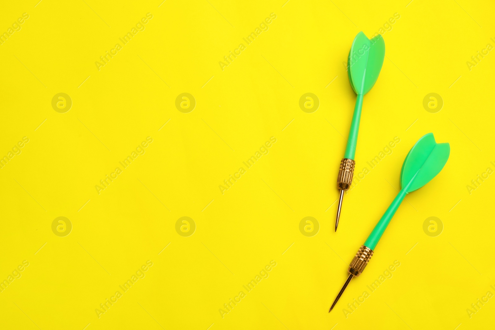 Photo of Green dart arrows on yellow background, flat lay with space for text