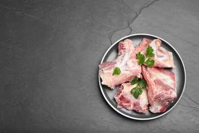 Photo of Plate with raw chopped meaty bones and parsley on black table, top view. Space for text