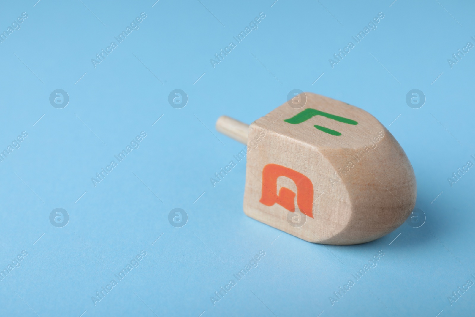 Photo of Hanukkah traditional dreidel with letters He and Pe on light blue background, closeup. Space for text