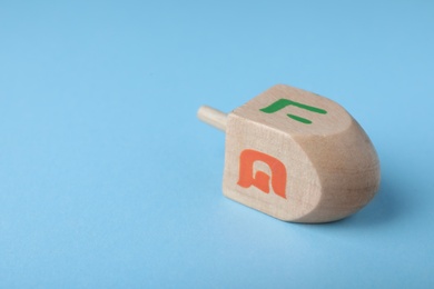 Photo of Hanukkah traditional dreidel with letters He and Pe on light blue background, closeup. Space for text