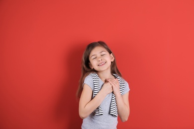 Portrait of girl holding hands near her heart on color background