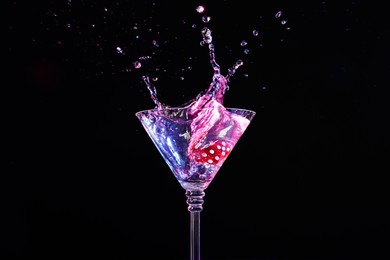 Casino dice falling into glass of alcohol drink on black background