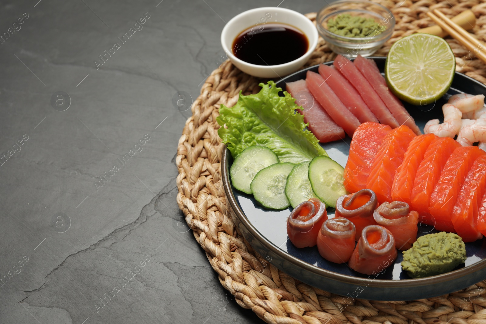 Photo of Tasty salmon slices, shrimp, cucumber and tuna on black table, space for text. Delicious sashimi set