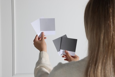 Photo of Woman choosing paint shade for wall indoors, focus on hands with color sample cards. Interior design