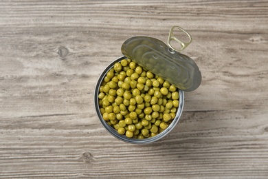 Photo of Open tin can of peas on wooden background, top view