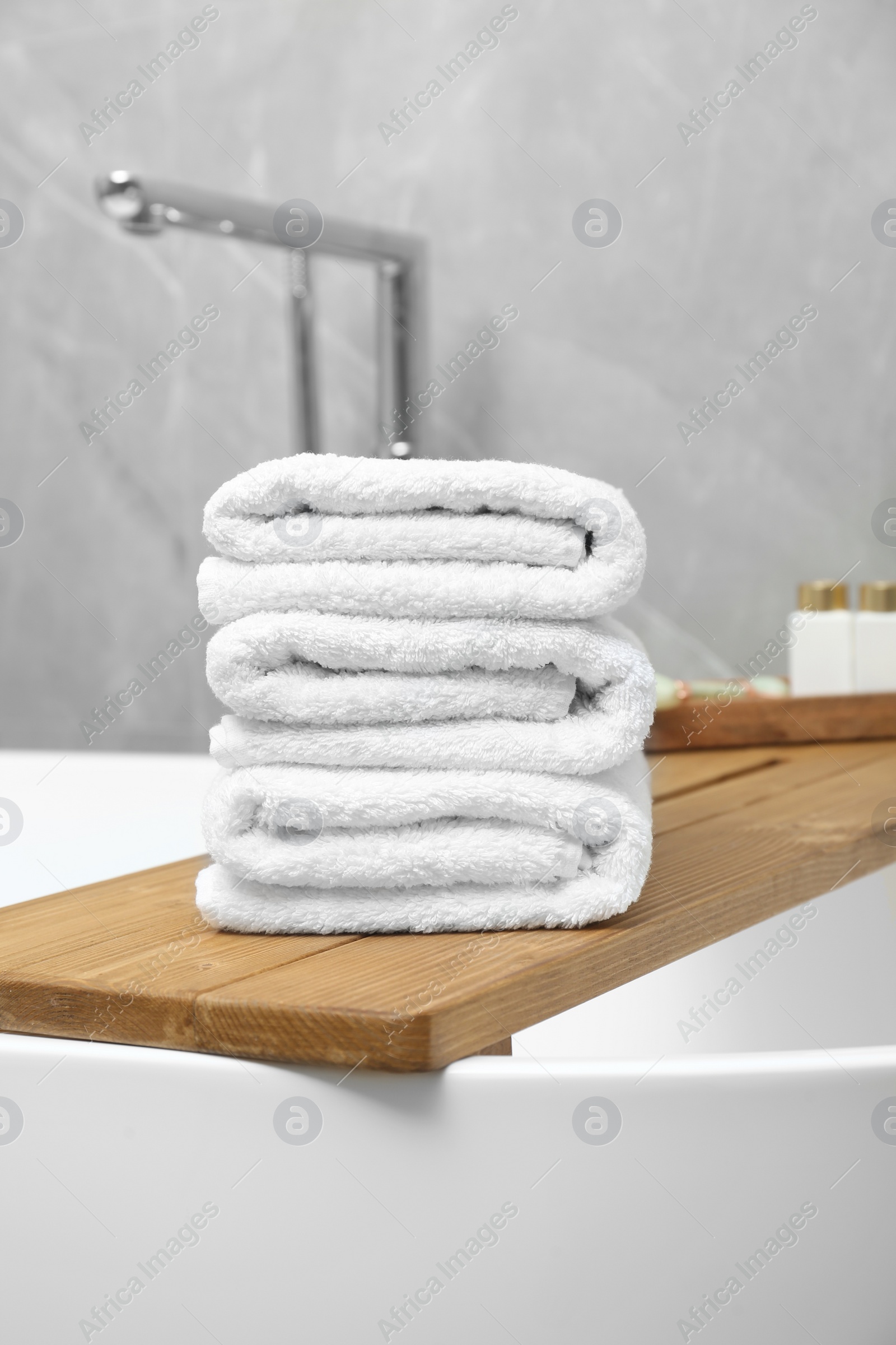 Photo of Stacked bath towels and personal care products on tub tray in bathroom