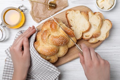 Photo of Woman cutting homemade braided bread at white wooden table, top view. Traditional Shabbat challah