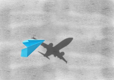 Flying paper plane and shadow of a real airplane on grey background