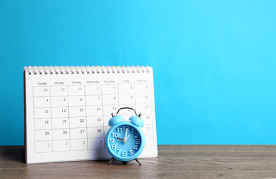 Photo of Calendar and alarm clock on wooden table against light blue background. Space for text