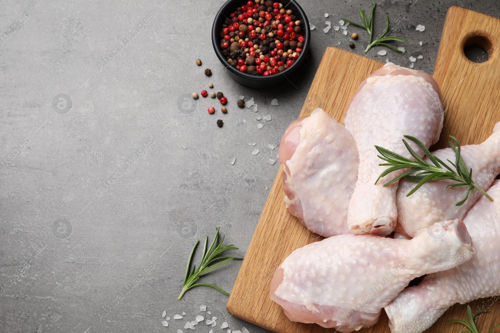Photo of Raw chicken drumsticks with rosemary and spices on grey table, flat lay. Space for text