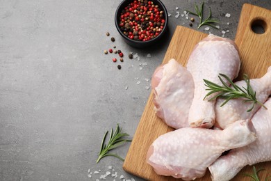 Photo of Raw chicken drumsticks with rosemary and spices on grey table, flat lay. Space for text