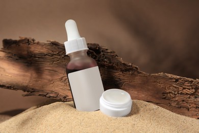 Photo of Cosmetic products and tree bark on sand against brown background