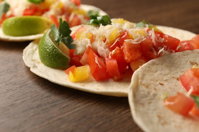 Delicious tacos with vegetables and lime on wooden table, closeup