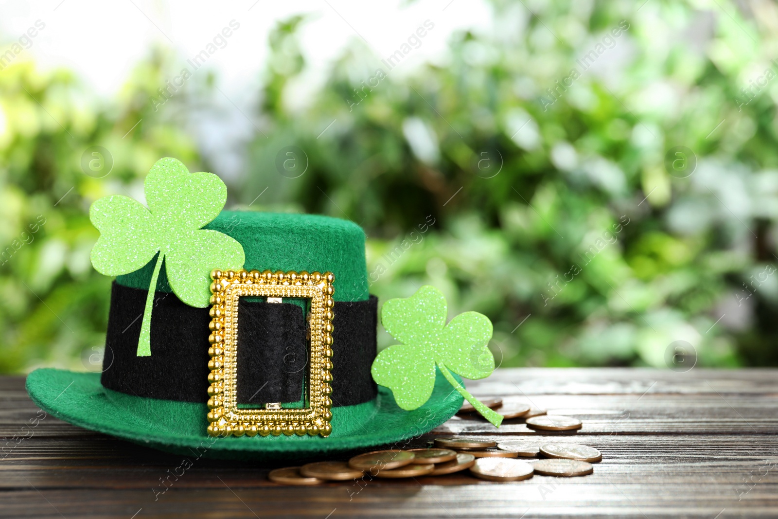 Photo of Green leprechaun hat, clover leaves and gold coins on wooden table, space for text. St Patrick's Day celebration