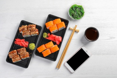 Flat lay composition with sushi rolls, smartphone and space for text on white wooden table. Food delivery