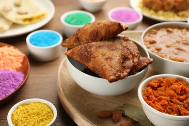 Photo of Traditional Indian food and color powders on wooden table, closeup. Holi festival celebration