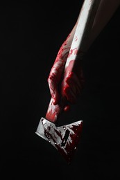 Man holding bloody axe on black background, closeup