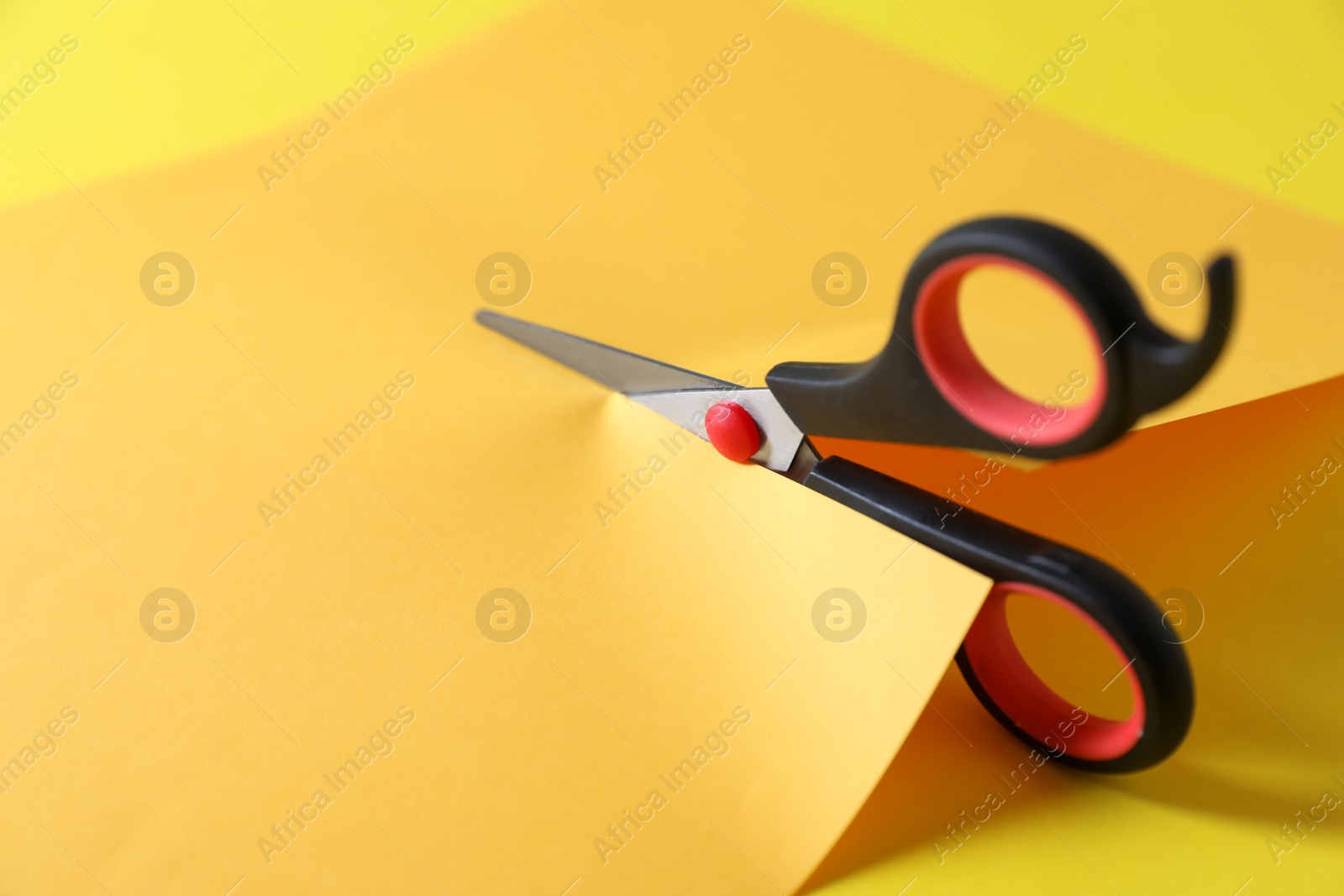 Photo of Scissors cutting color paper on yellow background, closeup