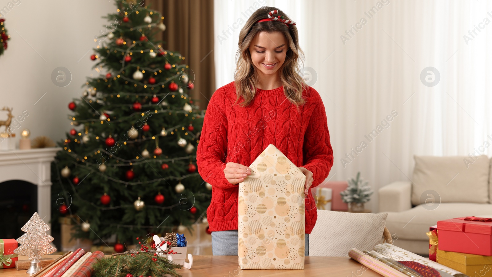 Photo of Beautiful young woman wrapping Christmas gift at home